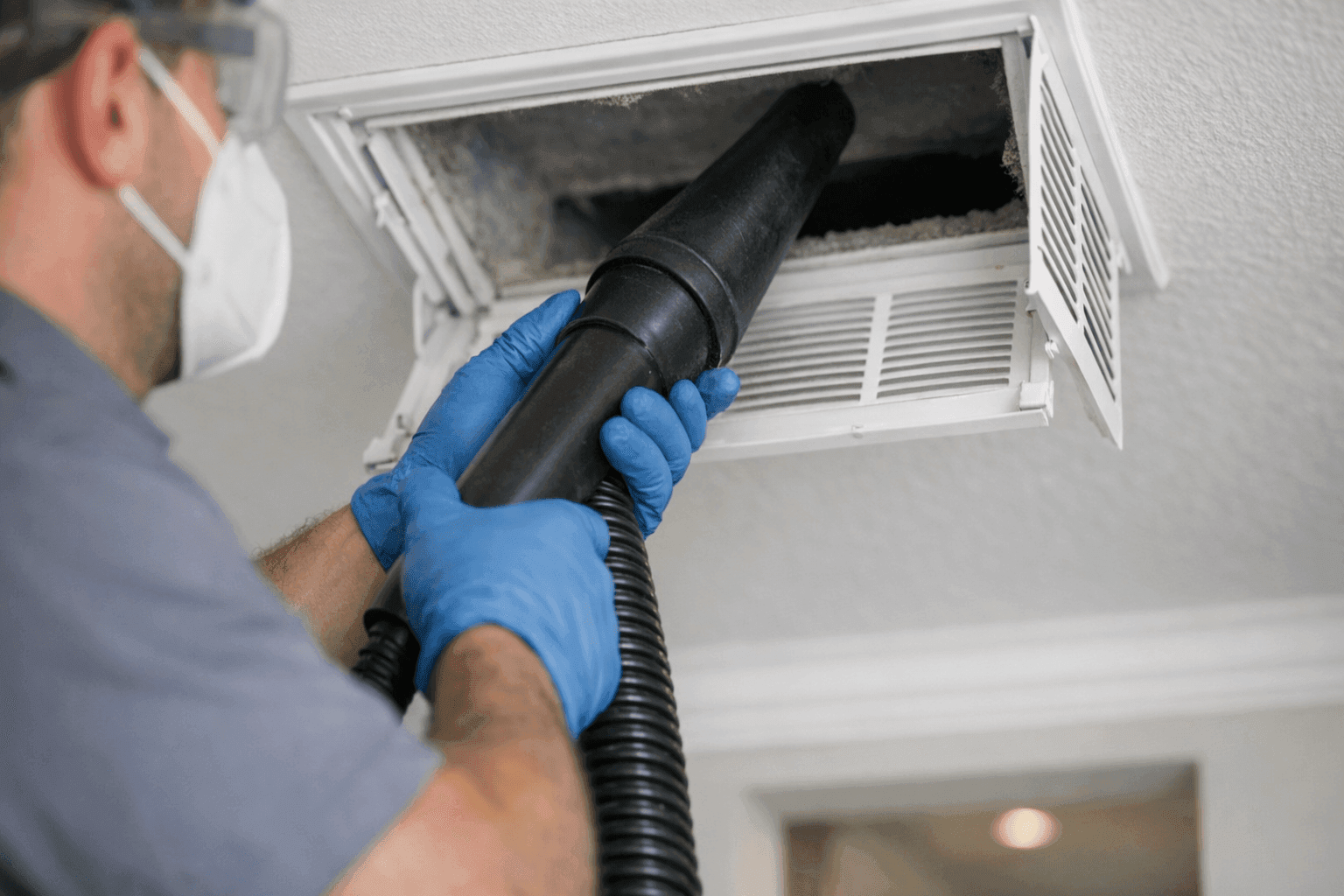 Technician operating duct cleaning vacuum tool in home vent
